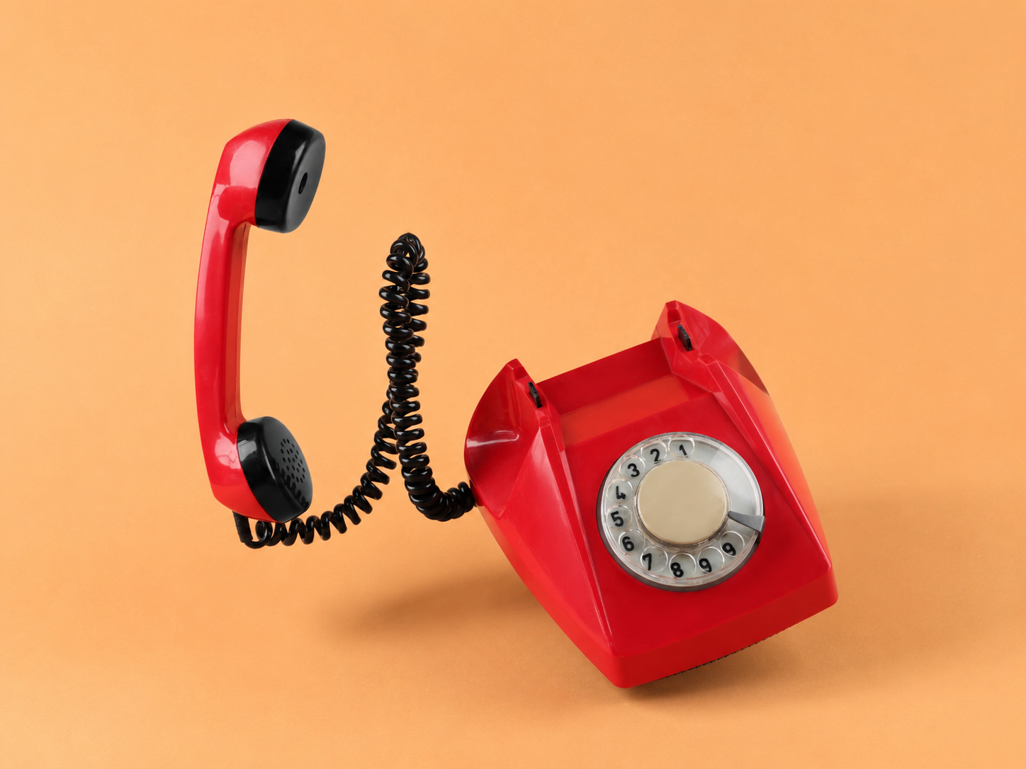 A red rotary telephone with the handset lifted